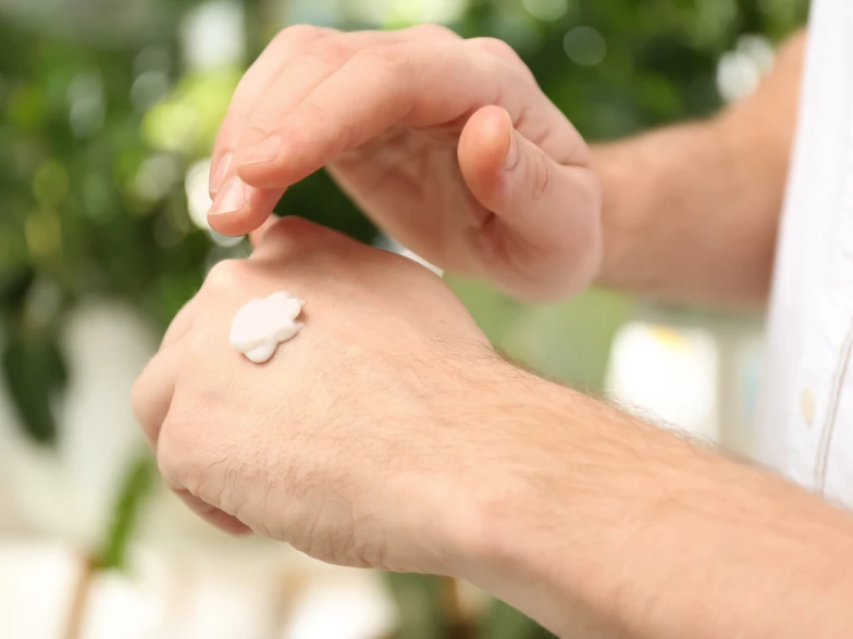 A close up of a person's hands, applying cream on the dorsal of the left hand.